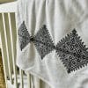 Plaid blanc avec broderie Fessi noir posé sur un lit bébé