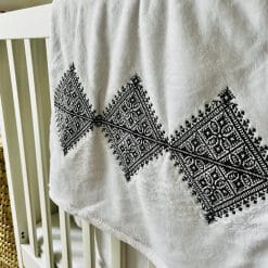 Plaid blanc avec broderie Fessi noir posé sur un lit bébé